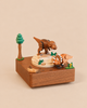 A Wooden Dinosaur Music Box featuring a T-Rex on a raised platform and a triceratops standing below, decorated with a small tree and greenery.