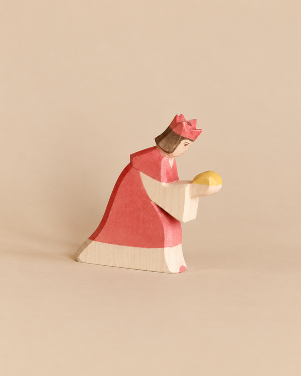 Ostheimer Red King With Crown: a handcrafted wooden toy figure of a king in a red robe and crown, kneeling and holding a yellow orb for imaginative play.