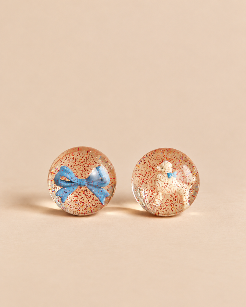 Konges Sloejd Glitter Bouncing Ball Set - Poodle & Bow featuring two clear bouncing balls filled with red glitter, one containing a blue bow and the other a white poodle figurine.