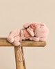 A Maileg Plush Sleeping Bunny With Harness featuring a flower accessory on its head and a matching leash, resting on a wooden stool.