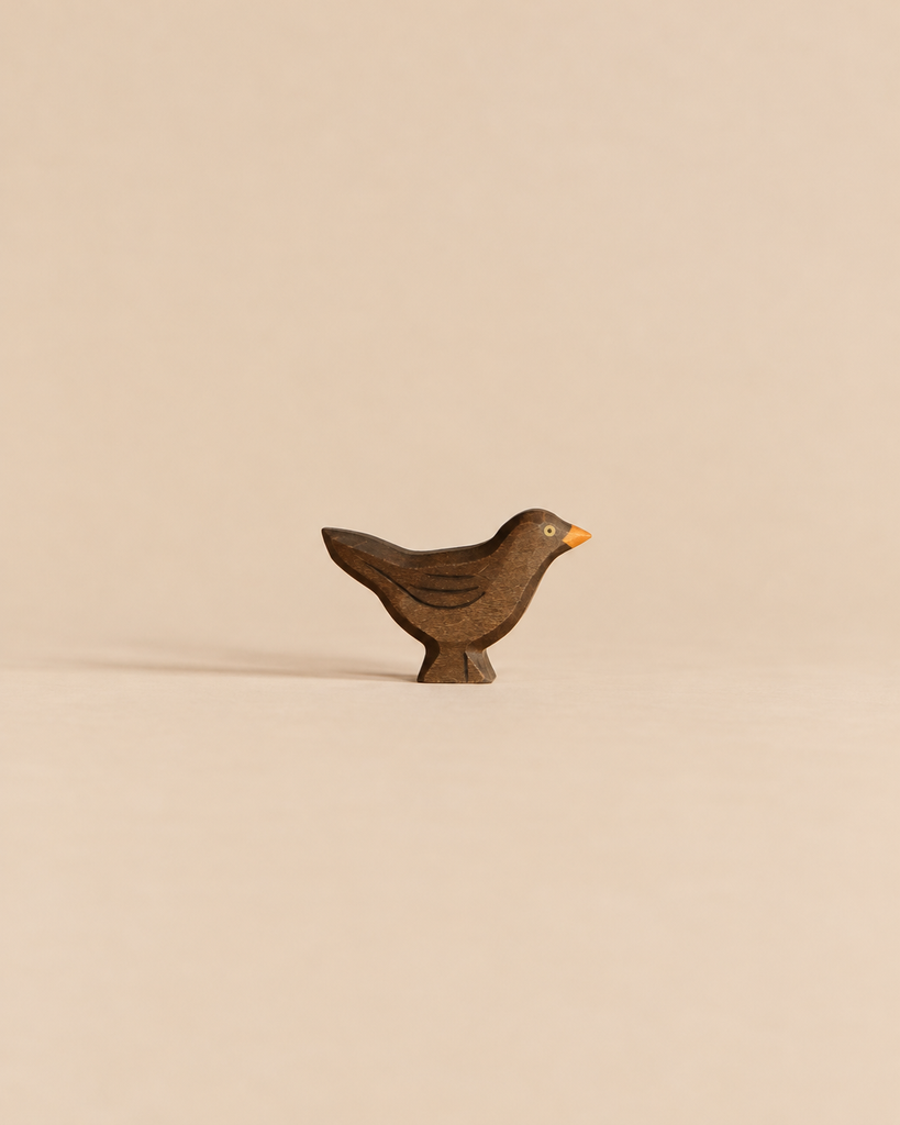 Handmade Holzwald Bird - Blackbird, a small, dark wooden bird figurine with a yellow beak crafted as a sustainable toy.