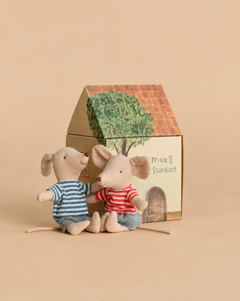 Two Maileg mice in striped shirts and shorts sit in front of a small cardboard house featuring a Maileg Garden Tea Set and other furniture.