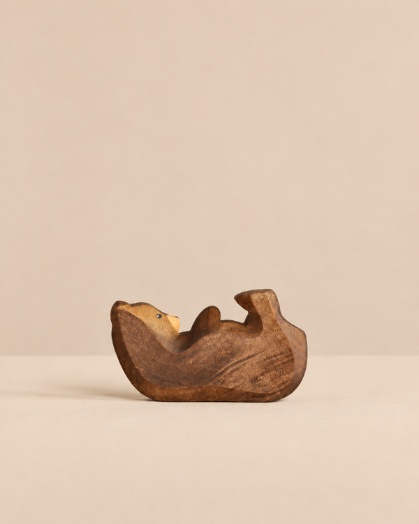 A small, hand-carved wooden Handmade Holzwald Bear Cub - Lying resting on its back, perfect for imaginative play.