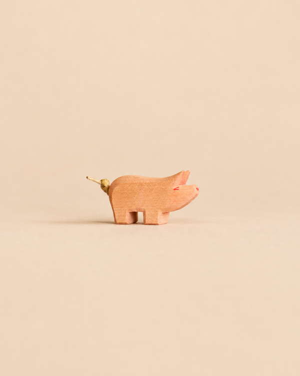 Small handcrafted wooden Ostheimer Piglet figurine with a knotted string tail, perfect for imaginative play.