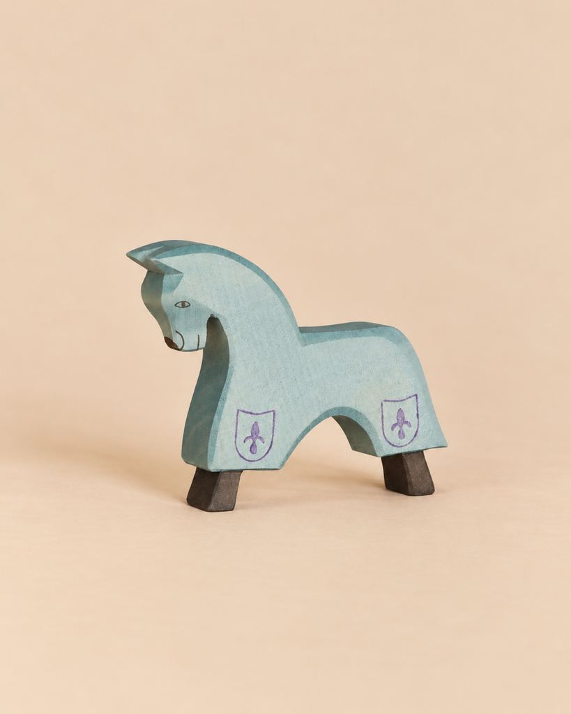 An Ostheimer Blue Horse for Knight handcrafted from wood, featuring a light blue body, purple fleur-de-lis emblems on its flanks, and dark brown hooves.
