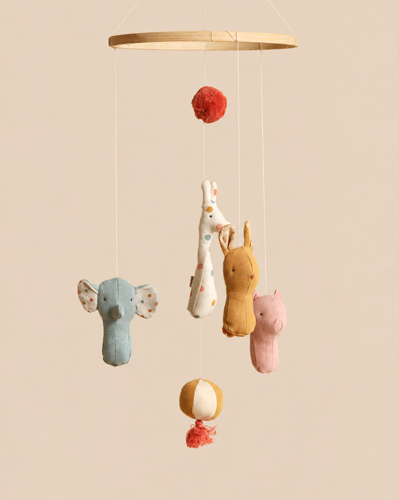 Maileg Lullaby Friends Mobile featuring a wooden hoop with hanging plush elephant, giraffe, rabbit, and pig toys, decorated with pom-poms and a striped ball to complement nursery decor.