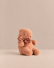 A small, dusty-pink, soft Maileg Teddy Bear Plush, Mini - Vintage Rose wearing a plaid bow around its neck.