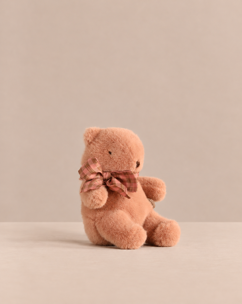 A small, dusty-pink, soft Maileg Teddy Bear Plush, Mini - Vintage Rose wearing a plaid bow around its neck.