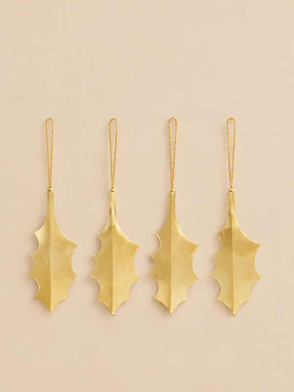 Four gold-colored brass Ferm Living Holly Leaf Ornaments - Set of 4 - Brass with thin hanging chains, arranged in a row against a light background as festive holiday décor.