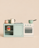 A Maileg Kitchen Counter, Mouse Size, featuring a stove, sink, and open shelving holding a toy can of tomatoes, mugs, and a saucepan.
