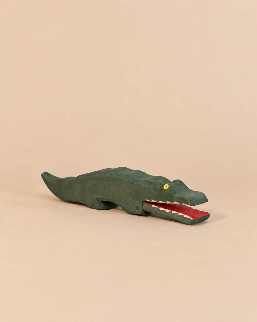 An Ostheimer Crocodile handcrafted wooden toy with a green body, yellow eye, and open red mouth showing white teeth, perfect for imaginative play.