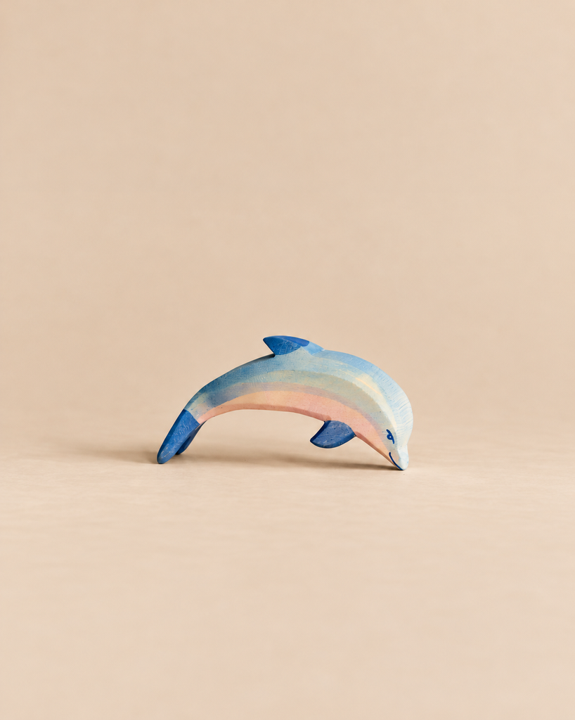 An Ostheimer Dolphin, Head Low wooden toy painted in shades of blue and pink, positioned with its head pointed downward.