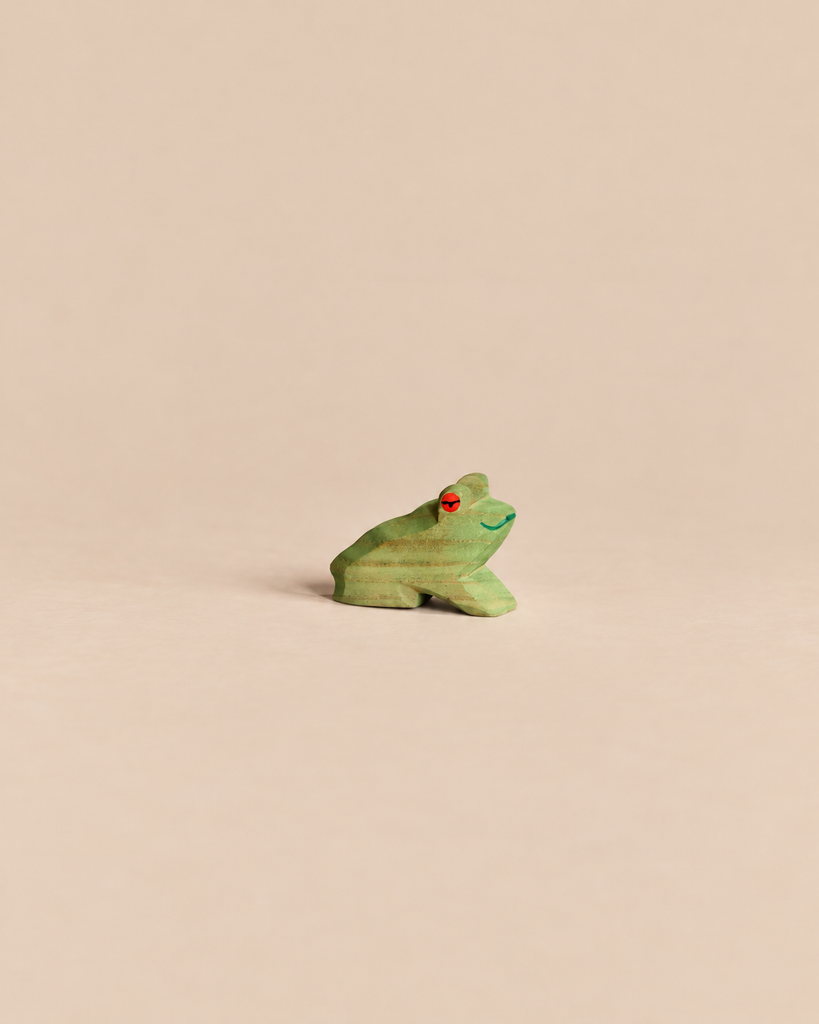 Ostheimer Frog Sitting, a small handcrafted wooden frog in a seated position with a green body and a red eye.