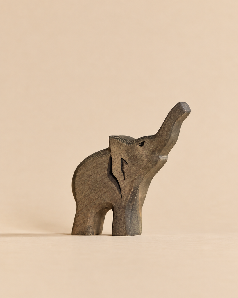 A sustainable wooden Handmade Holzwald Baby Elephant figurine with its trunk raised, perfect for imaginative play.