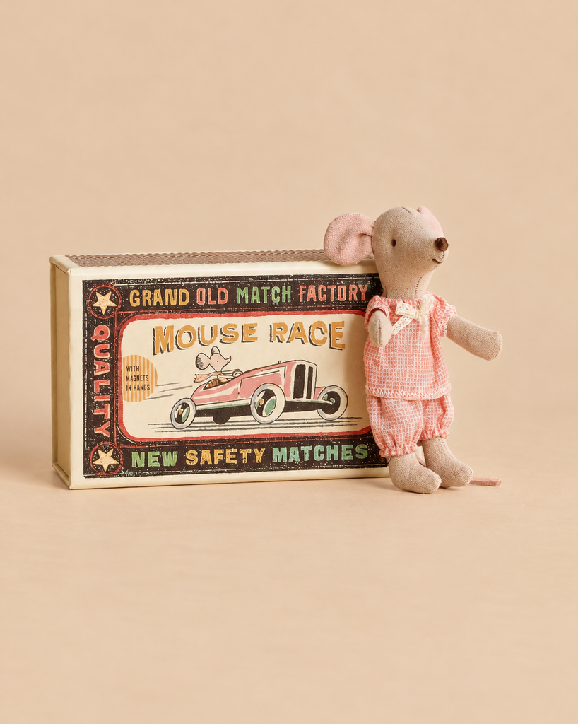 A Maileg Little Sister Mouse in Matchbox wearing pink pajamas stands next to a matchbox labeled “Mouse Race.”