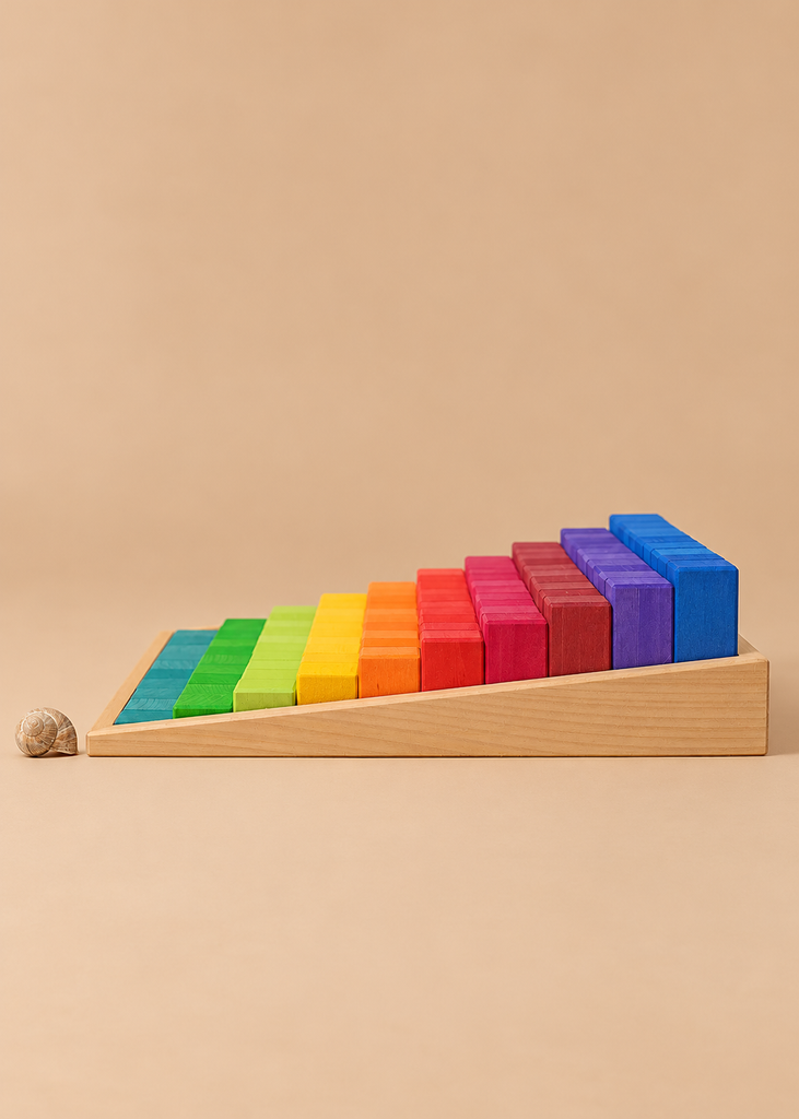 Grimm’s Stepped Counting Blocks - Large, a set of rainbow-colored wooden blocks in ascending heights arranged on a slanted tray, with a small snail shell resting on the surface nearby.