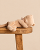 A small, soft Maileg Sleeping Kitten Plush, Small - Cream Peach, with closed eyes, lying on its side on a wooden stool.