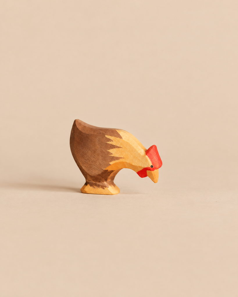 An Ostheimer Hen Picking - Brown handcrafted wooden toy with brown feathers and a red comb, depicted with its head lowered to the ground in a pose typical of imaginative play.