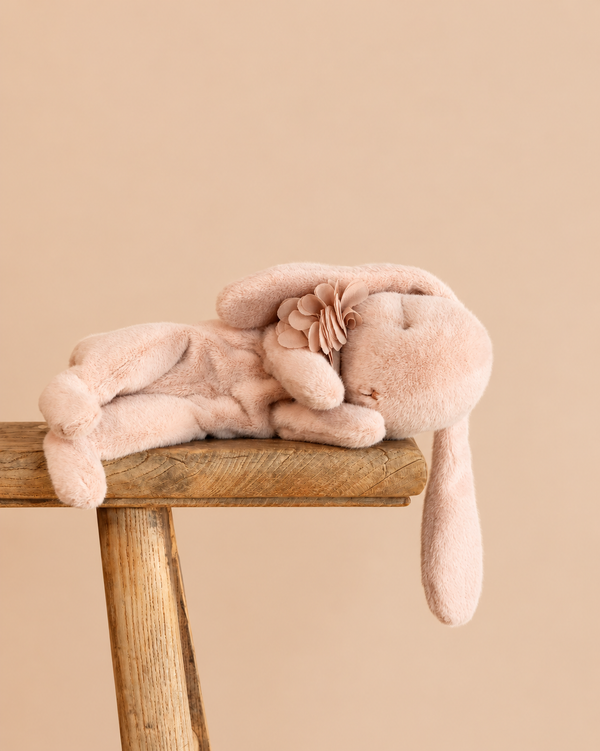 A soft, pink Maileg Plush Sleeping Bunny - Powder with a fabric flower on its head, resting on a wooden stool.