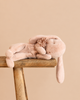 A soft, pink Maileg Plush Sleeping Bunny - Powder with a fabric flower on its head, resting on a wooden stool.