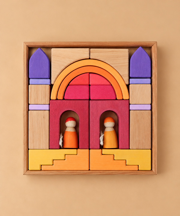 Wooden blocks in shades of yellow, orange, red, and purple arranged in a wooden tray to form an arched gateway with two small wooden peg dolls inside, part of a Grimm’s Building World - Desert Sand set for imaginative play.