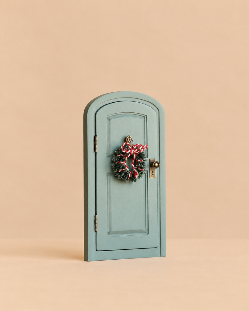 A miniature arched sage green Maileg Christmas Door Set, Mouse, decorated with a small wreath tied with red and white string.