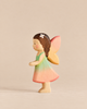 A small fairy figurine from the Handmade Holzwald Fairy Tale Set, wearing a green and pink dress with brown hair, a white flower accessory, and pink wings.