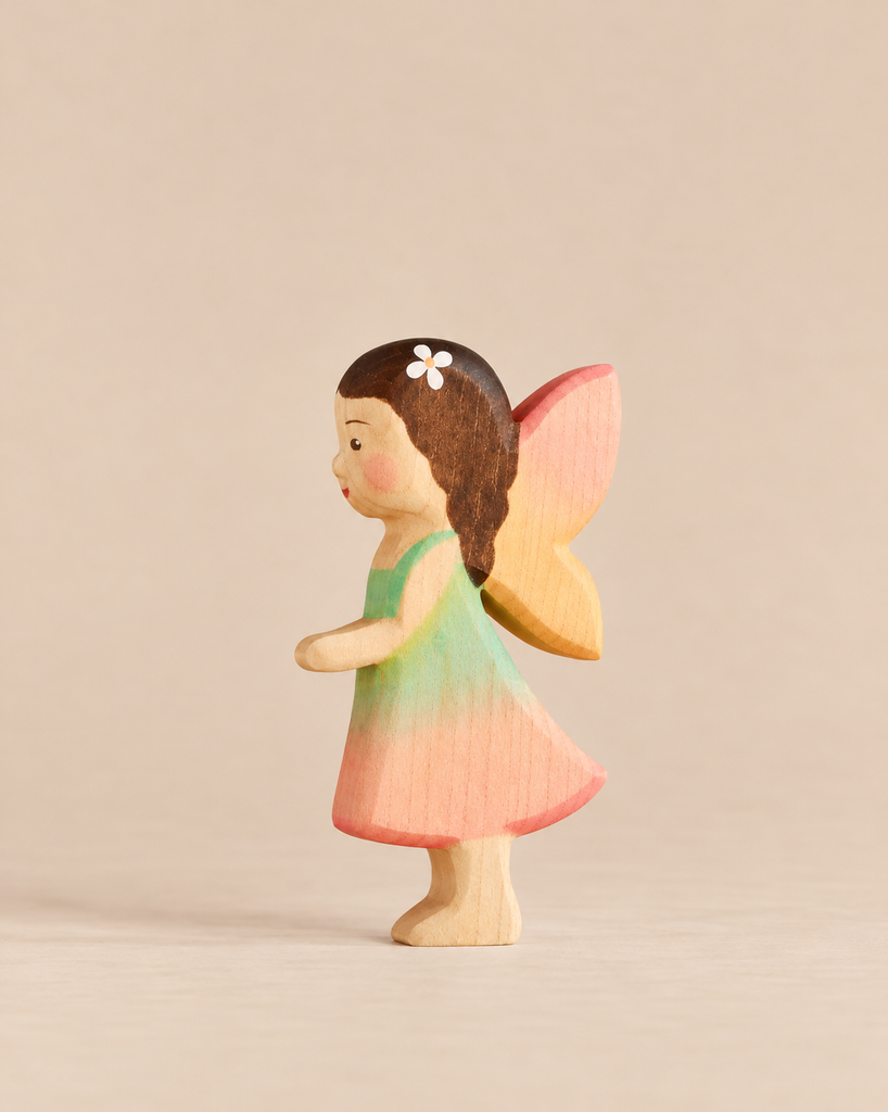 A small fairy figurine from the Handmade Holzwald Fairy Tale Set, wearing a green and pink dress with brown hair, a white flower accessory, and pink wings.