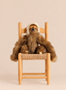 A realistic Sloth Stuffed Animal with long brown fur and a light-colored face sits on a small wooden chair.