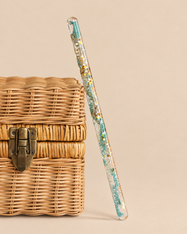 Konges Sloejd Magical Glitter Wand - Green Mix leaning against a small wicker box.