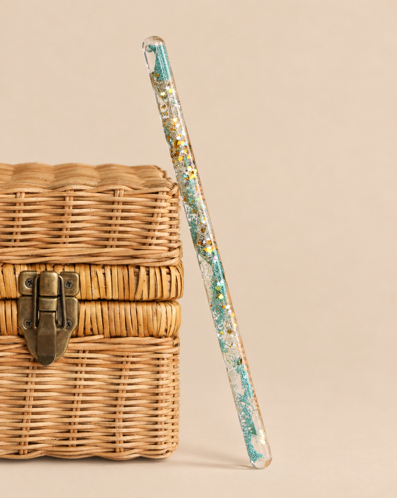Konges Sloejd Magical Glitter Wand - Green Mix leaning against a small wicker box.