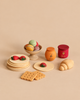 The Sabo Concept Handmade Wooden Bakery Set - Desserts includes a stack of pancakes with strawberry slices, a bowl of macarons, two jars of jam, a croissant, and two square biscuits.
