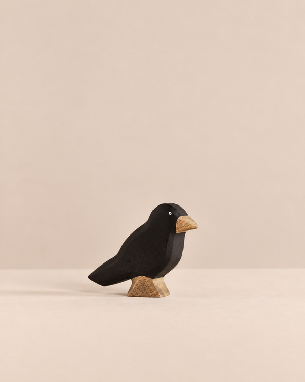 A Handmade Holzwald Bird - Raven figurine with a black body, a tan beak, and a light-colored base.