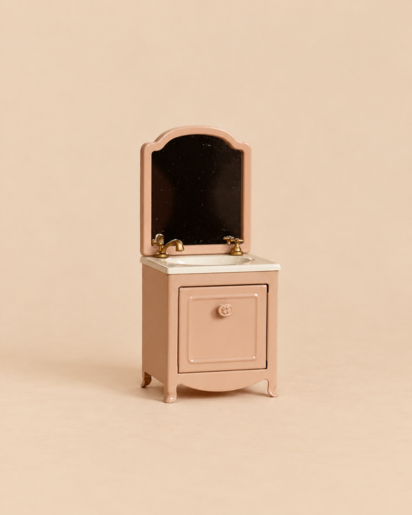 Maileg Sink Dresser With Mirror, Mouse - Dark Powder, a miniature pink bathroom vanity featuring a sink, two gold-toned faucets, and an attached mirror.