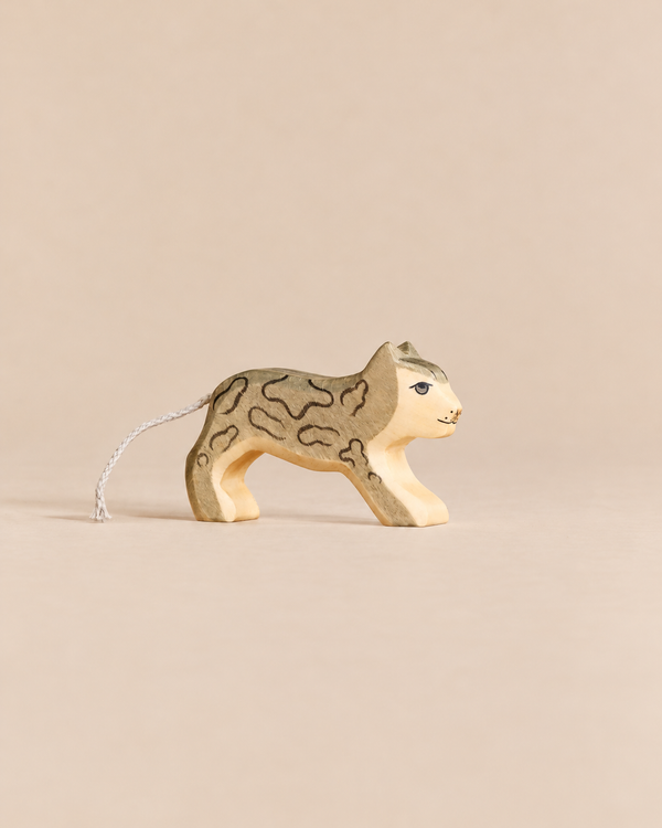 Handmade Holzwald Small Snow Leopard, a hand-carved wooden toy with painted spots and a string tail, designed for imaginative play.