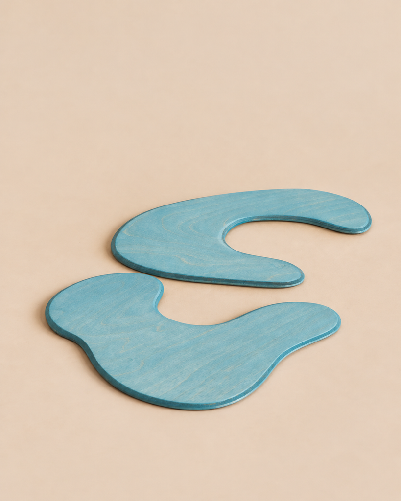 Two blue, irregularly shaped handcrafted wooden Ostheimer Pond Plates - Set of 2 positioned on a plain light background.