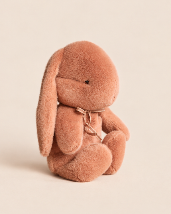 A dusty rose Maileg Plush Bunny, Medium - Vintage Rose sits upright with a small ribbon tied around its neck.