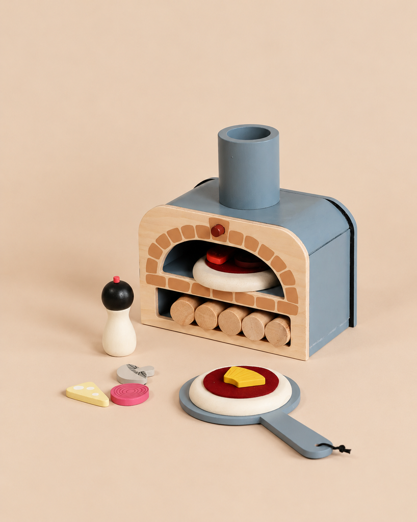 A Wooden Make Me A Pizza Set featuring a wooden toy pizza oven, pepper grinder, and pizza toppings on a plain surface for pretend play.