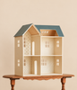 A Maileg Dollhouse, House of Miniature with a blue roof, open interior rooms, and patterned wallpaper, sitting on a wooden table.
