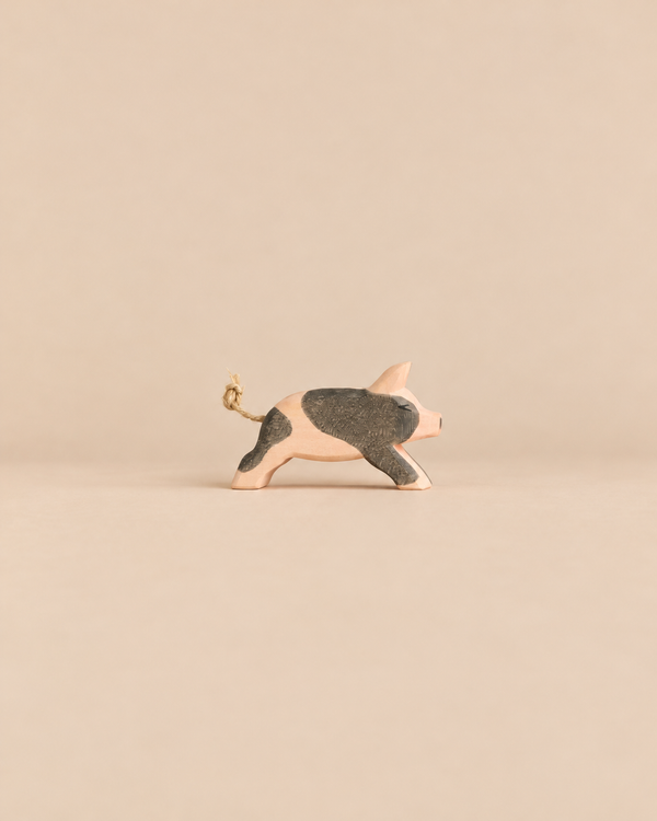 Ostheimer Spotted Piglet - Running: a handcrafted wooden toy piglet in a running pose with dark patches and a knotted string tail.