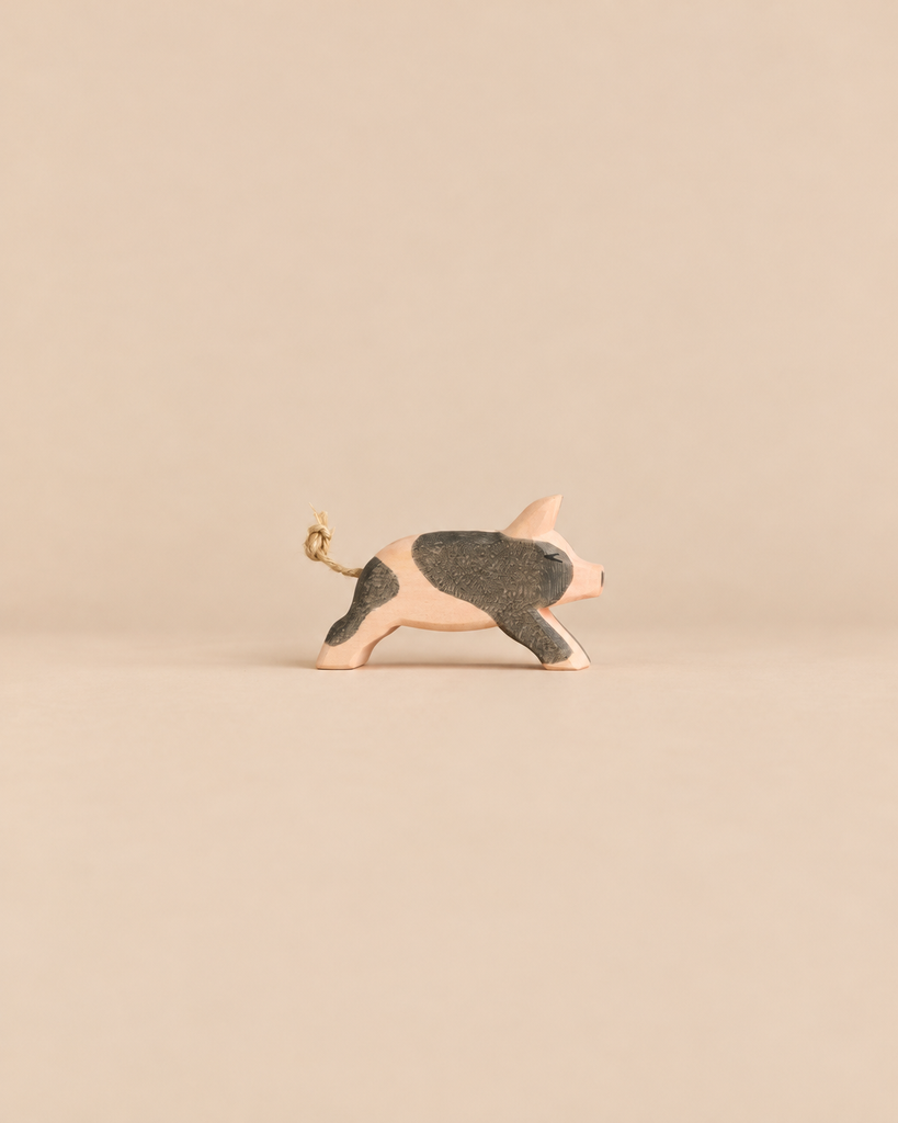 Ostheimer Spotted Piglet - Running: a handcrafted wooden toy piglet in a running pose with dark patches and a knotted string tail.