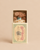A Maileg Sleepy Wakey Baby Mouse in Matchbox - Blue, tucked into its vintage matchbox with a patterned blanket and wearing a blue collar.