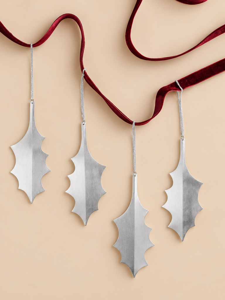 A set of four Ferm Living Holly Leaf Ornaments - Set of 4 - Silver, featuring silver-plated holly leaves with silver chains hanging from a decorative dark red ribbon.