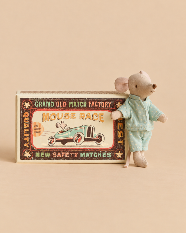 A Maileg Little Brother Mouse in Matchbox stands next to its decorative matchbox, which features a vintage-style “Mouse Race” illustration, while the mouse wears light blue polka-dot pajamas.