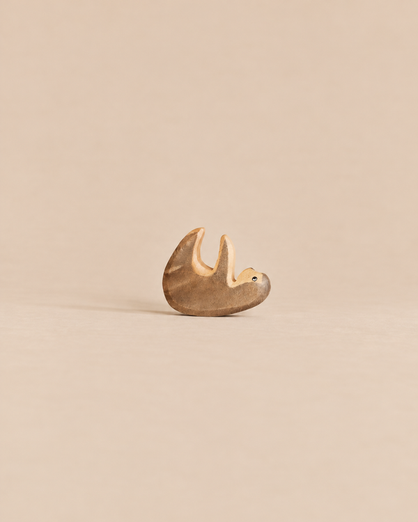 A small, sustainable Handmade Holzwald Small Sloth wooden figurine hanging from a branch.