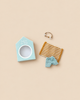 The Maileg Beach Bundle for Big Brother includes a small cardboard beach hut box, a striped towel, plaid shorts, and a tiny gold-tone wire ring.