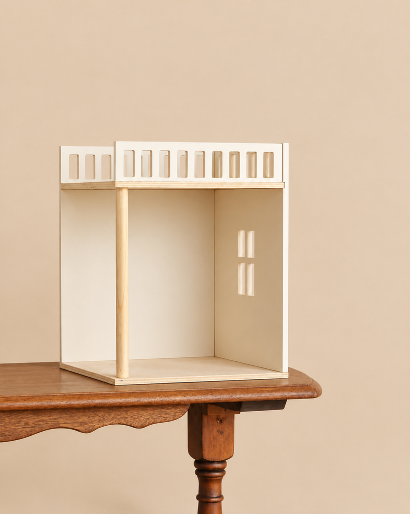 A Maileg House of Miniature Bonus Room - Bedroom, featuring a small, open-fronted wooden room with a balcony railing, resting on a wooden table as a dollhouse accessory.