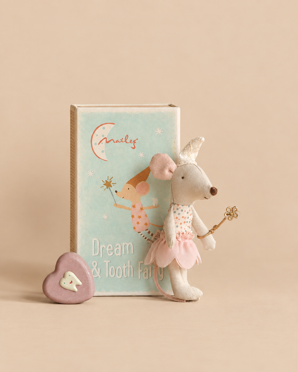 A Maileg Tooth Fairy Mouse, Little Sister toy dressed in a star wand costume stands next to its rectangular storage box and a small heart-shaped trinket with a tooth illustration, perfect as a kids bedtime gift.