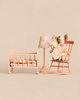 Two Maileg Big Sister and Me Nursery Set mice sit in a pink rocking chair next to a miniature cradle and a small table lamp.