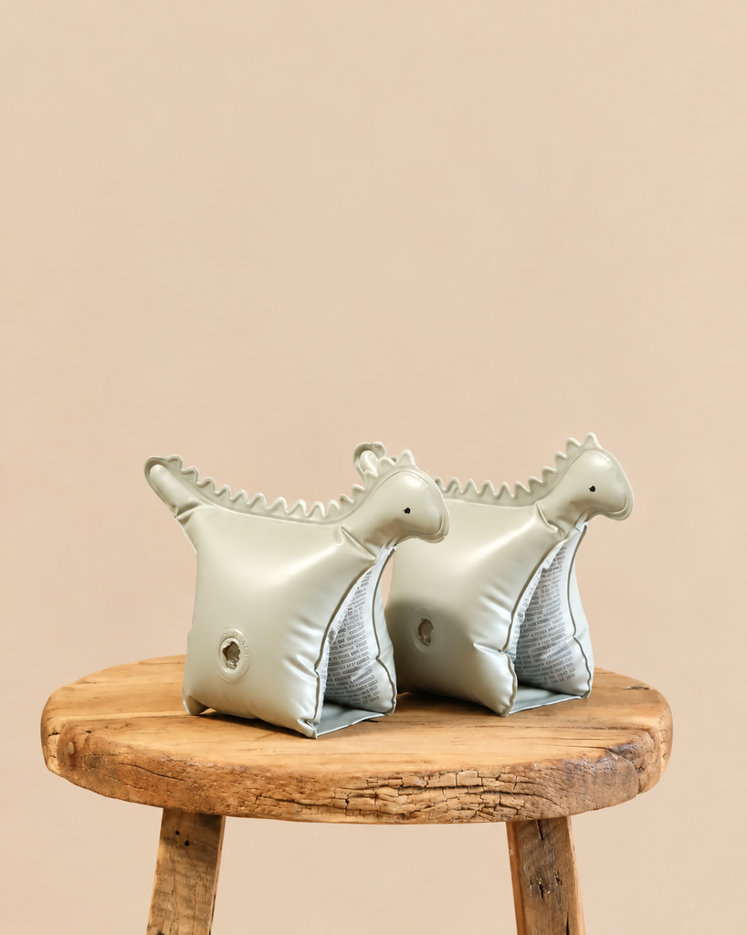 Two pale green Inflatable Water Wings - Dinosaur Shape - Final Sale resting on a wooden stool.
